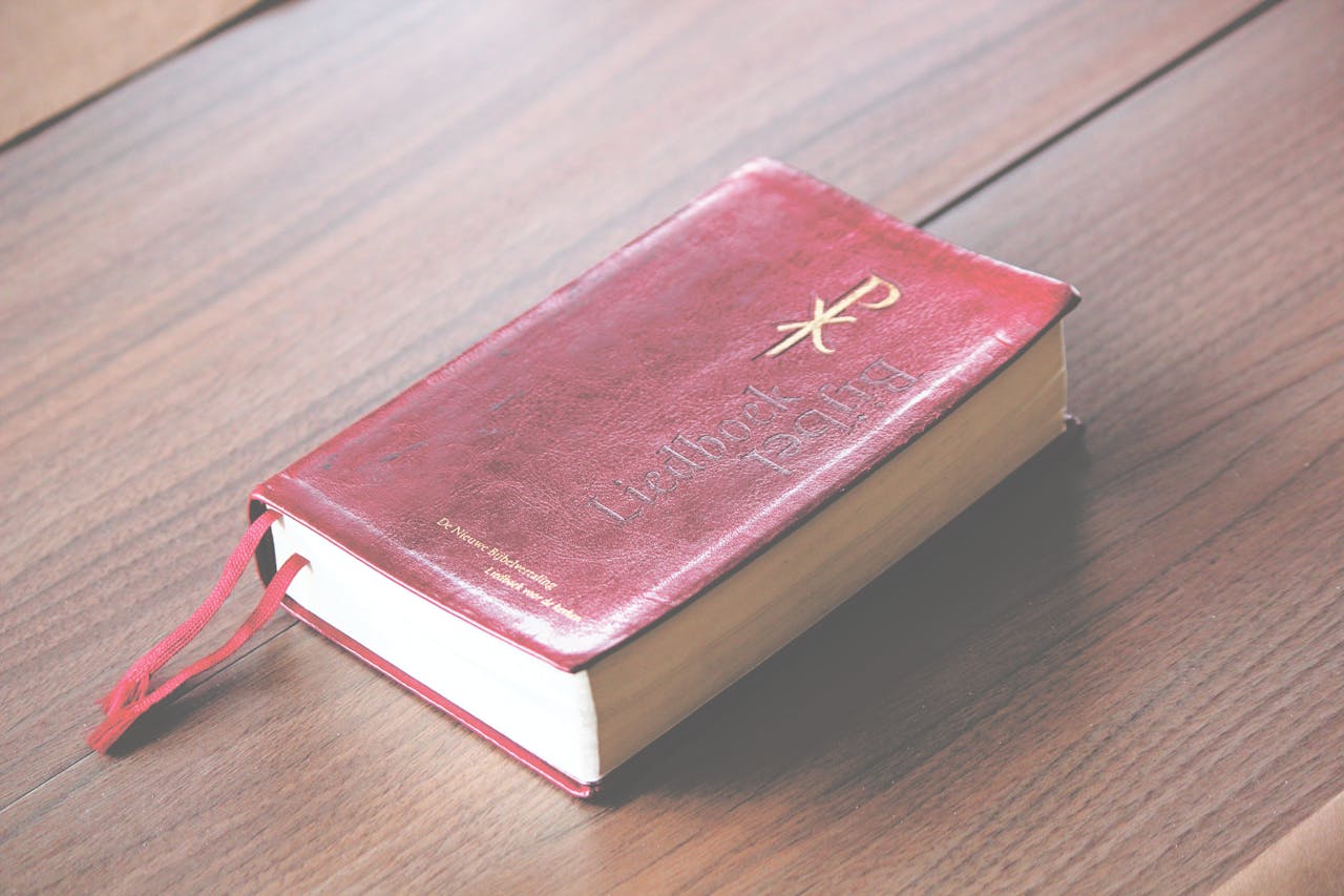 A red vintage-style Bible with ornate design lies on a wooden table, symbolizing knowledge and spirituality.